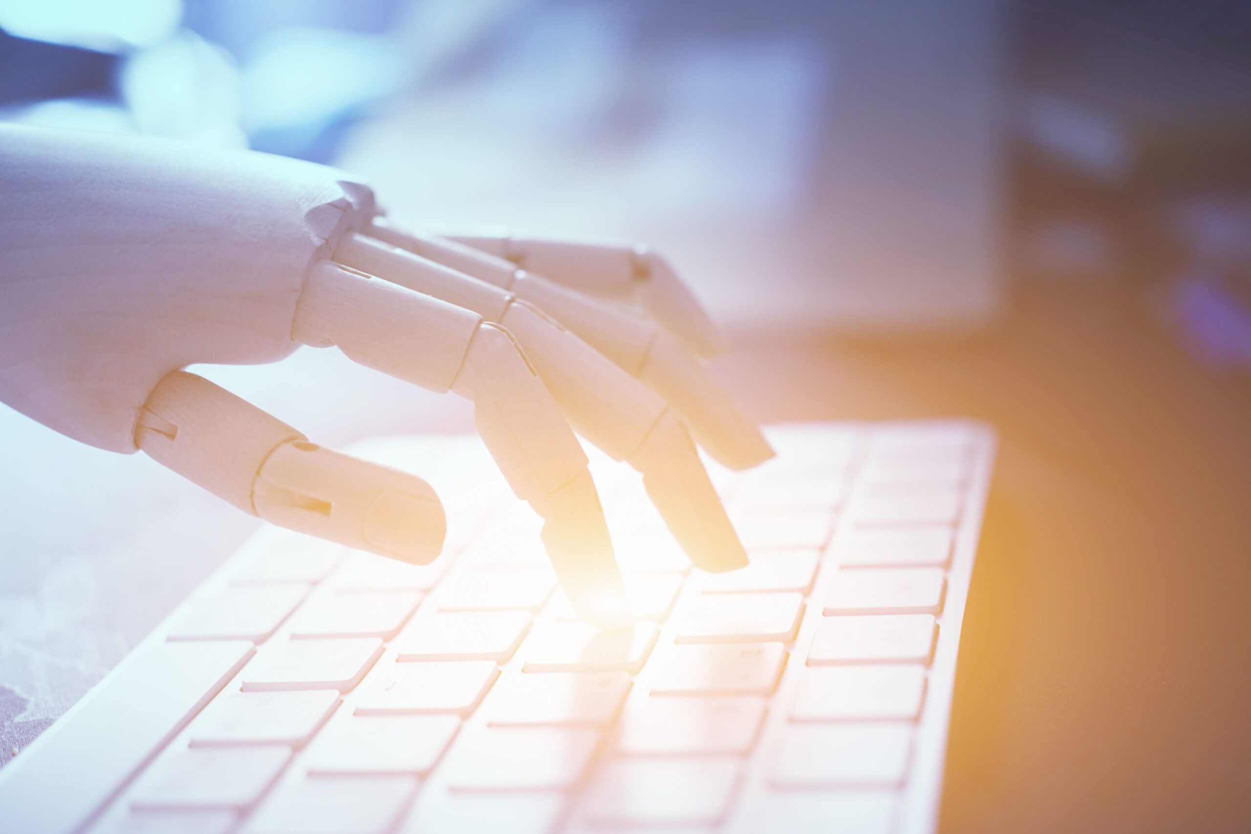 Künstliche Intelligenz, Robotter Hand auf Computertastatur, helle Farben, Tageslicht durchs Fenster